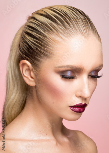 Closeup beauty portrait of young woman with makeup, hair straightened and caught in the back, isolated pink background.