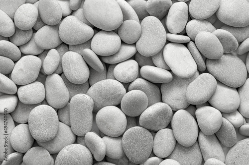 Grey and white stone background at the beach. Meditation concept during vacation. Round and smooth pebbles texture at daylight. Summer time near the sea. Cobblestone pattern. Rocks at the seashore.