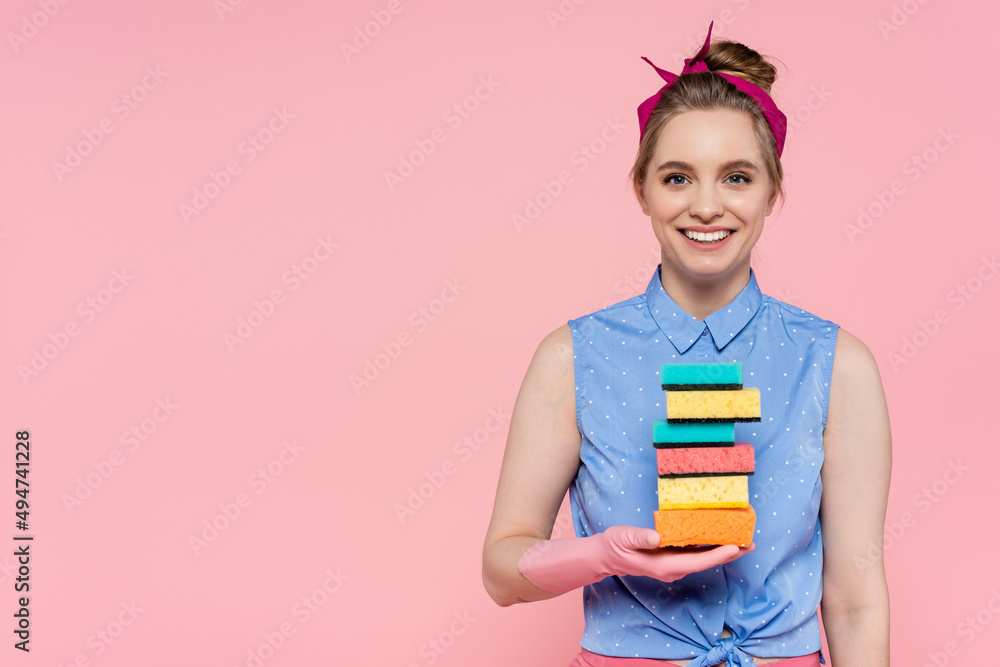 happy young woman in rubber gloves holding stacked sponges isolated on pink. happy young woman in rubber gloves holding stacked sponges isolated on pink.