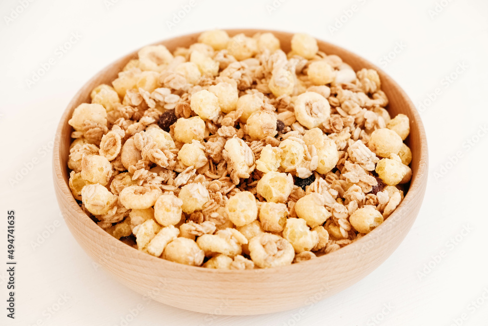 Dry muesli with cornflakes, nuts and raisins in a wooden bowl on a white background Dry muesli with cornflakes, nuts and raisins in a wooden bowl on a white background