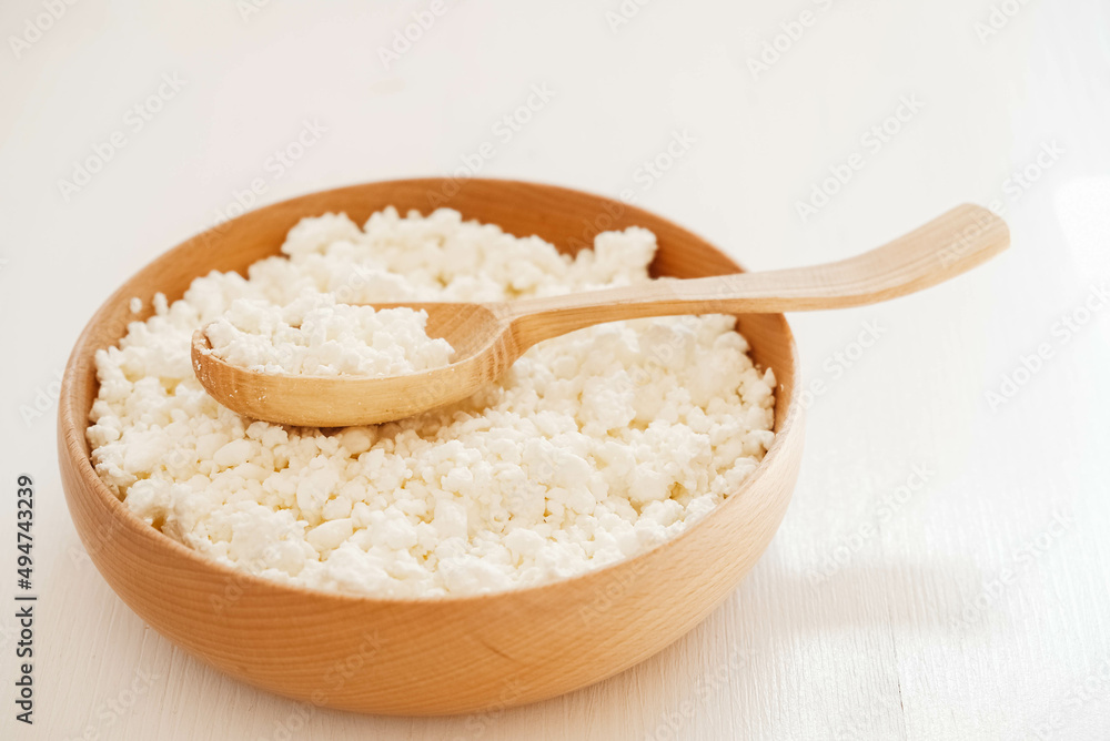 Cottage cheese in a wooden plate with a spoon on a white background
