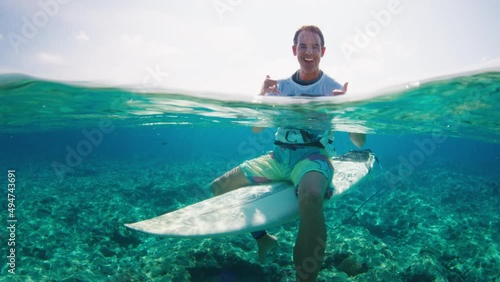 Adult man surfer sits on the surf board in the tropical ocean and shows shaka sign photo