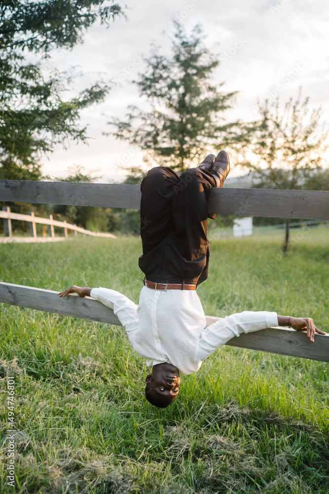 Handsome african man hanging upside down on wooden fence