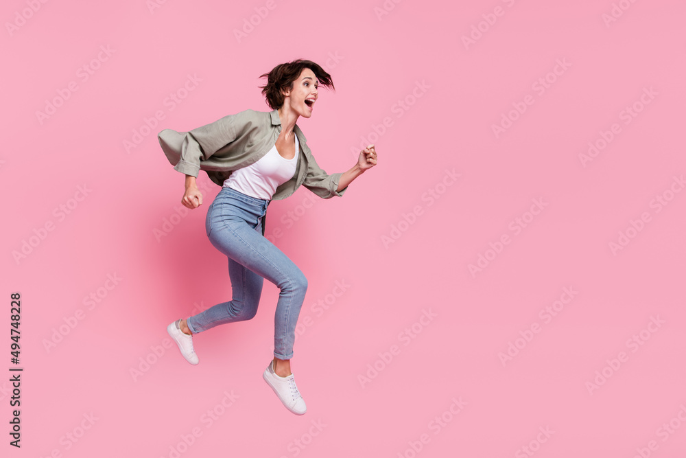 Full size profile side photo of young excited lady runner jumper rush speed look empty space isolated over pink color background Full size profile side photo of young excited lady runner jumper rush speed look empty space isolated over pink color background