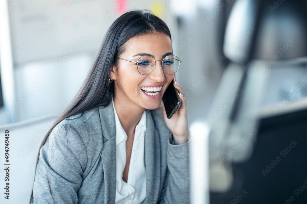 Beautiful business woman talking on mobile phone while working with her laptop in the office. Beautiful business woman talking on mobile phone while working with her laptop in the office.