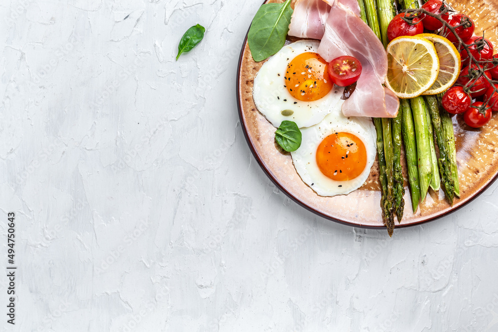 Tasty breakfast. Sunny side up eggs with green asparagus, bacon, ham and and cherry tomatoes. Healthy balanced food. Top view, above, banner Tasty breakfast. Sunny side up eggs with green asparagus, bacon, ham and and cherry tomatoes. Healthy balanced food. Top view, above, banner