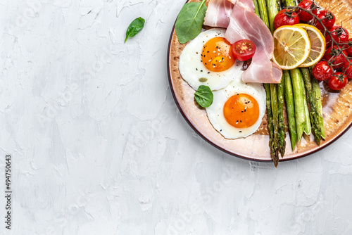 Tasty breakfast. Sunny side up eggs with green asparagus, bacon, ham and and cherry tomatoes. Healthy balanced food. Top view, above, banner