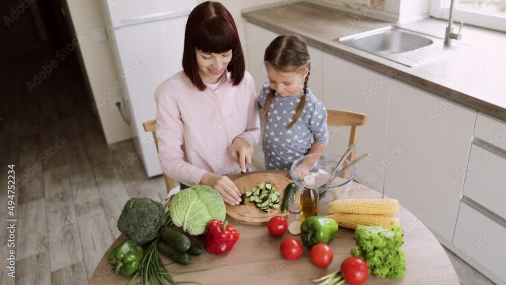 Top view of mother teach little preschooler daughter chop vegetables preparing salad for lunch together loving mom and small girl child cooking dinner together, kid helping mommy with food preparation Top view of mother teach little preschooler daughter chop vegetables preparing salad for lunch together loving mom and small girl child cooking dinner together, kid helping mommy with food preparation