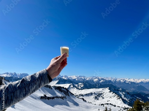 Hand of woman holding glass of eggnog against spectacular winter panorama in the Austrian Alps. Vorarlberg, Austria. photo