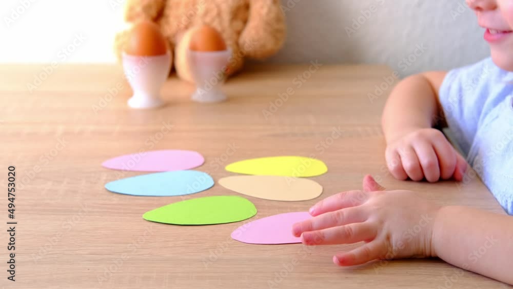 figures of eggs from colored cardboard on table, baby's hands show, count, small child counting on fingers, happy childhood and school concept, healthy food, traditional Easter holiday figures of eggs from colored cardboard on table, baby's hands show, count, small child counting on fingers, happy childhood and school concept, healthy food, traditional Easter holiday