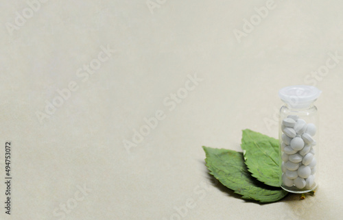 Transparent bottle with white pills and two leaves from wood on craft background