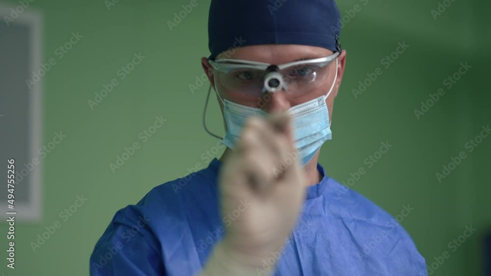 Portrait of serious concentrated male surgeon examining scalpel in slow motion. Caucasian expert man in uniform and surgical mask standing in operation room in hospital indoors. Medicine concept Portrait of serious concentrated male surgeon examining scalpel in slow motion. Caucasian expert man in uniform and surgical mask standing in operation room in hospital indoors. Medicine concept