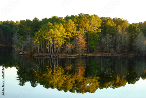 Light captures the top of green, yellow and orange trees. The trees are perfectly reflected in the mirror like surface of the surrounding lake photo