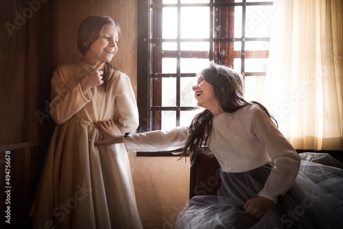 Fotografie Little girls in white vintage dresses inside a countryside cabin, smiling