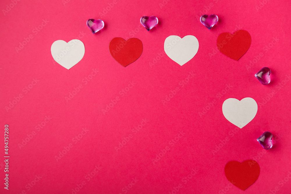 On a pink background, red and white hearts and heart-shaped pebbles.