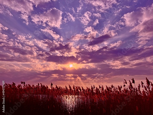 Sunset over field. Fantastic sunset in the sky clouds over lake. Surreal purple orange fiery dusk.