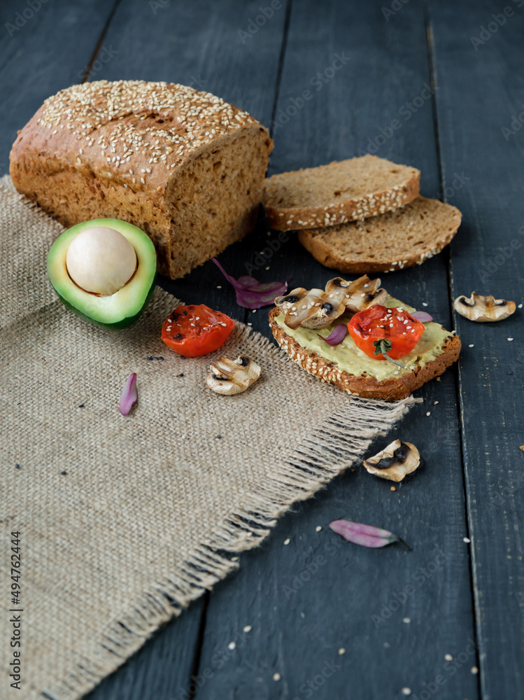 Avocado toast with grilled tomatoes and grilled mushrooms on dark wooden table. Healthy food and vegan diet concepts Avocado toast with grilled tomatoes and grilled mushrooms on dark wooden table. Healthy food and vegan diet concepts