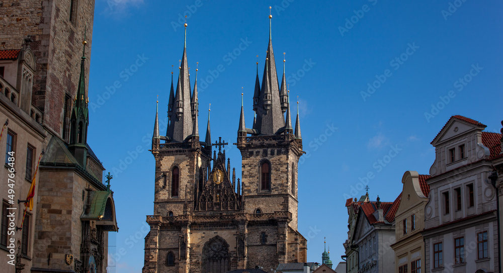 View of the spiers of the Church of Our Lady before Týn. The spiers of the church stand out against the azure blue sky. To the left and right historic buildings are visible.
