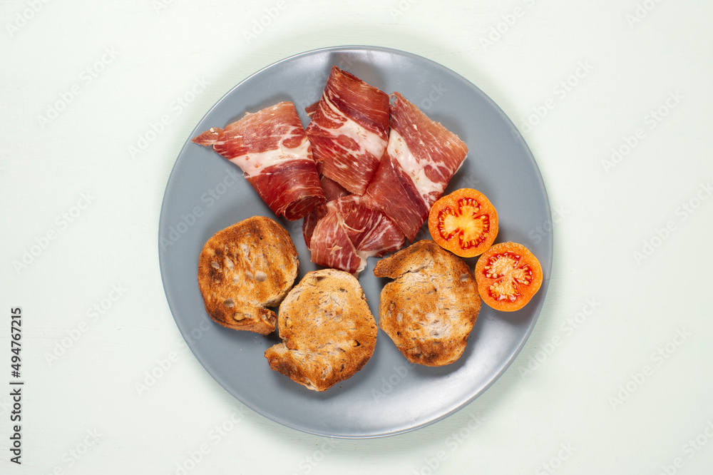 Tostadas de pan, jamón y tomate de untar en plató gris sobre fondo verde laurel Tostadas de pan, jamón y tomate de untar en plató gris sobre fondo verde laurel