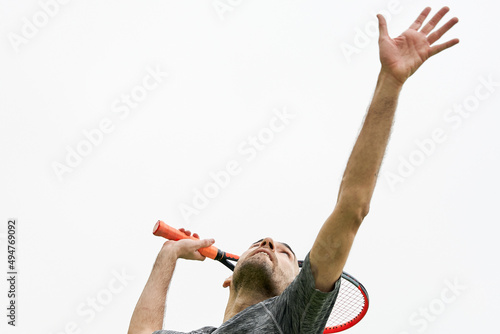 Bilde på lerret Young tennis player with grey t-shirt about to hit serve with racket over white