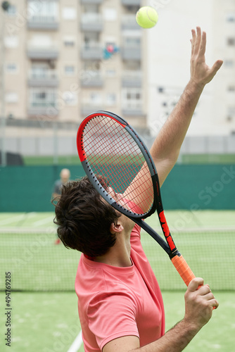 Vertical shot of young tennis player in pink t-shirt throws ball in the air before serve