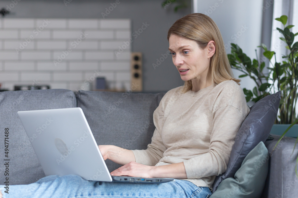Naklejka premium Beautiful woman at home sitting on sofa smiling and working on laptop
