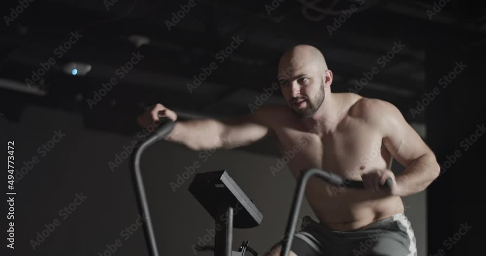 Muscular sportsman exercising on air bike Muscular sportsman exercising on air bike