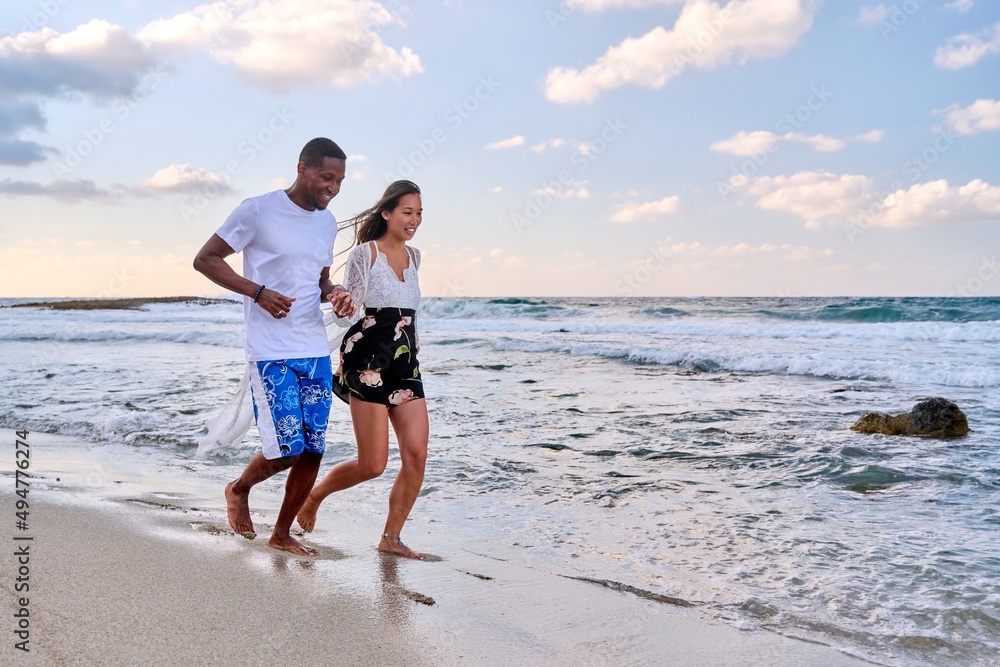 Young happy couple walking on the beach holding hands, copy space
