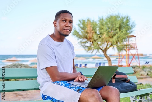 Young smiling male freelancer relaxing on beach, sitting on bench using laptop © Valerii Honcharuk