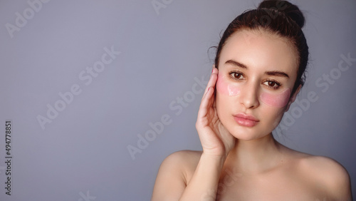 Woman, brunette with pink eye patches on a purple background, fresh face without makeup, natural color