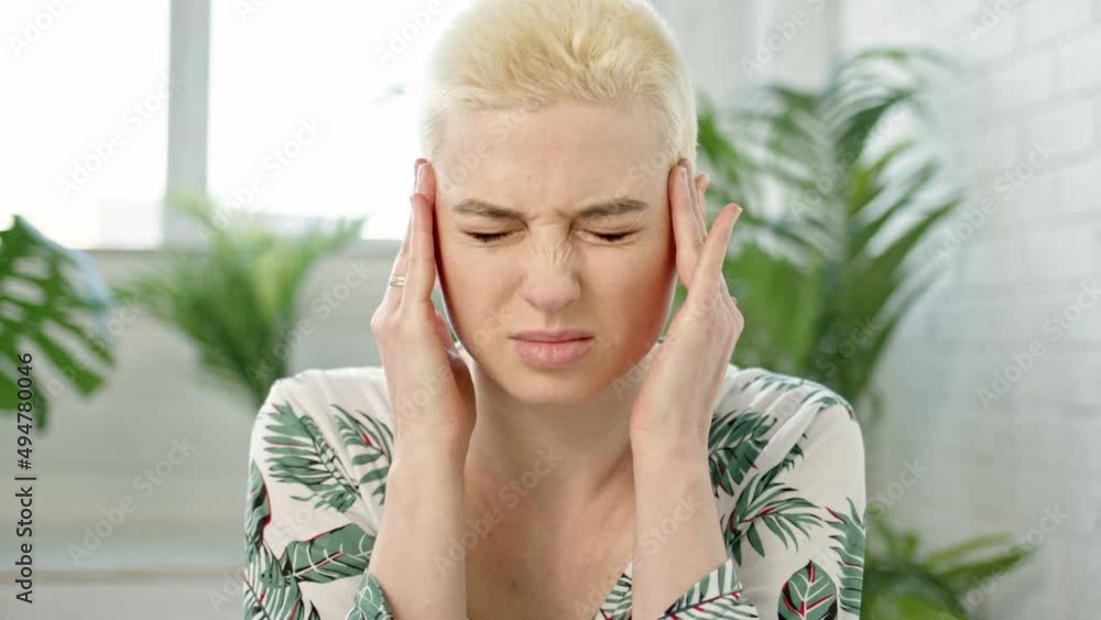 Close up young blond short hair woman with bun on her head is experiencing severe headaches