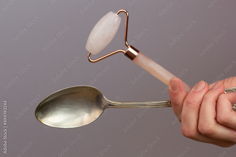Closeup of a rose quartz roller and a cold spoon – tools that can be used to depuff face in the morning.