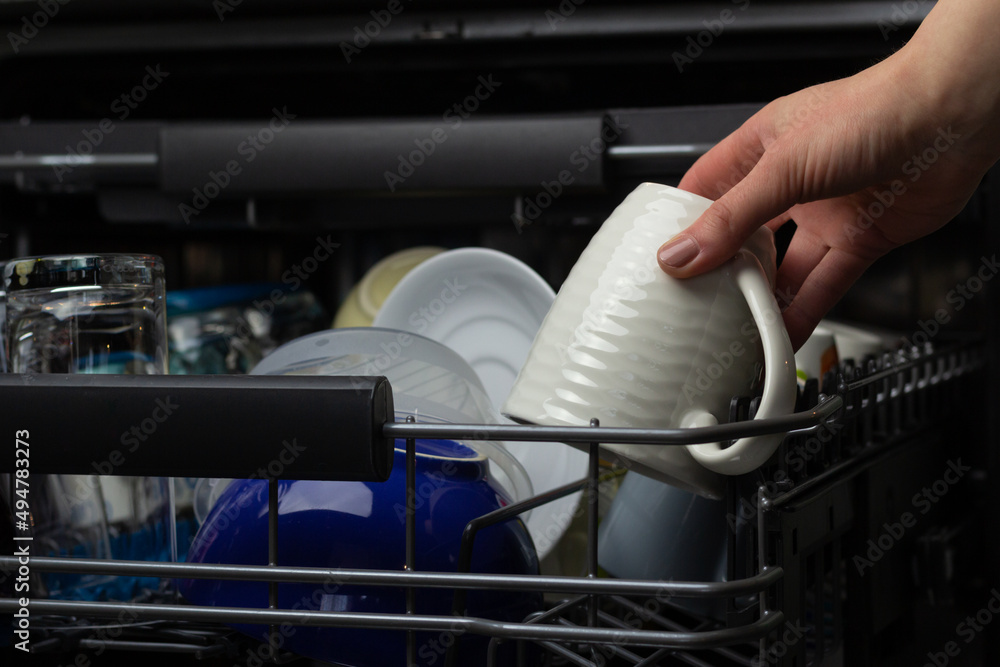 Closeup of a woman putting a mug to dishwasher.
