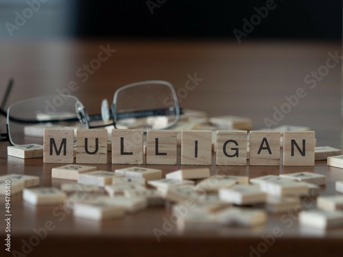 mulligan word or concept represented by wooden letter tiles on a wooden table with glasses and a book