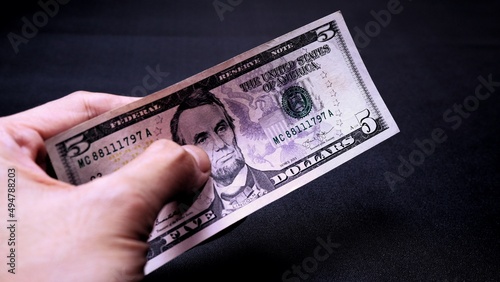 Businessman's hand holding American Dollar Banknotes, isolated on black background. Business Investment Economy Saving Loan Income Money and Finance concept. Five Dollar, 5 USD. Prosperity concept.