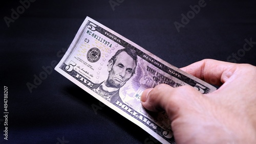 Businessman's hand holding American Dollar Banknotes, isolated on black background. Business Investment Economy Saving Loan Income Money and Finance concept. Five Dollar, 5 USD. Prosperity concept.