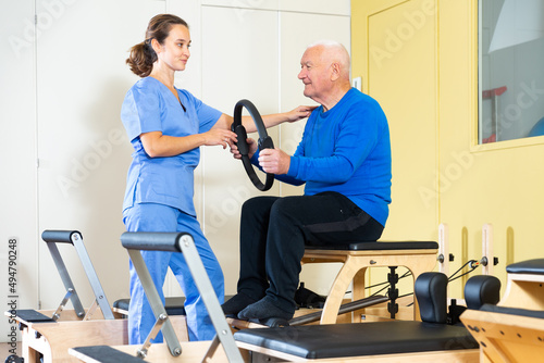 Healthcare professional helps an elderly man restore health with gymnastic ring in a pilates class