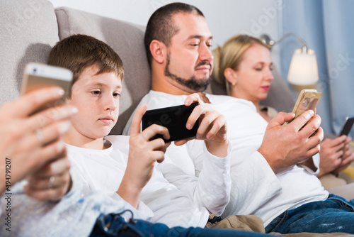 Parents and teen son using phones sitting on sofa at home