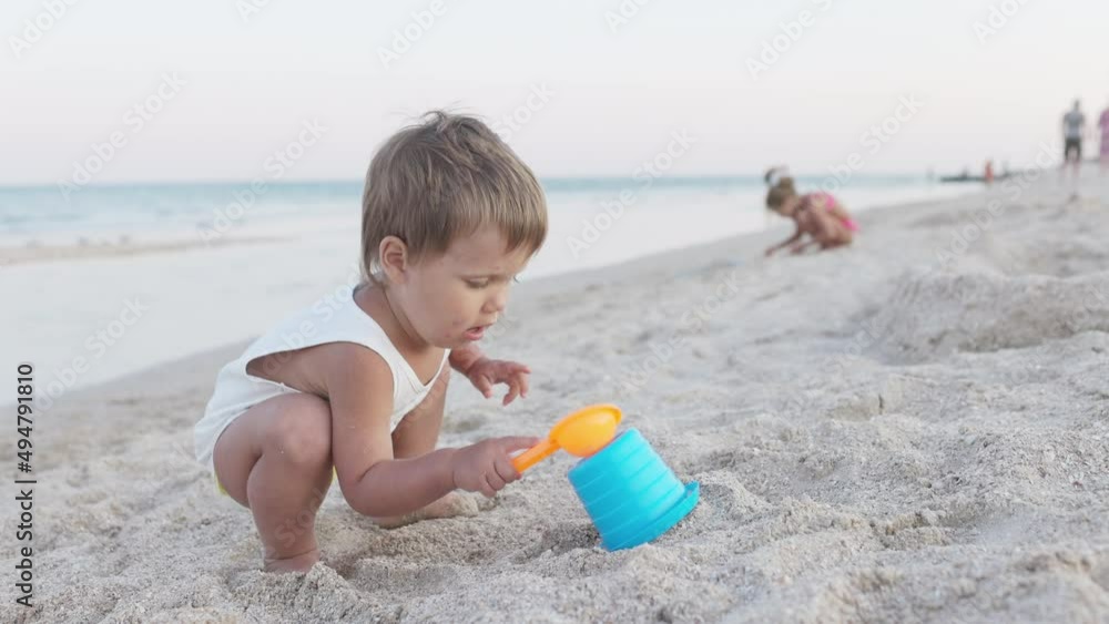 Boy playing with toys on the beach building beads and turrets smiling at someone behind the scenes on summer vacation Boy playing with toys on the beach building beads and turrets smiling at someone behind the scenes on summer vacation