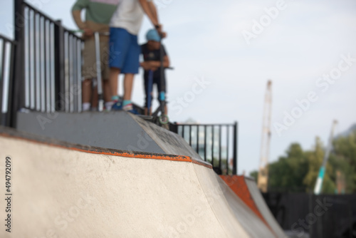 Skate park view with kids on a kick scooter doing tricks and stunts, boys in a skate park riding bmx bike and skate, playing and enjoying summer on new ramp, teenagers skateboarders and bmx riders