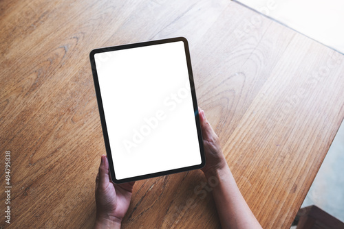 Top view mockup image of a woman holding digital tablet with blank white desktop screen on wooden table