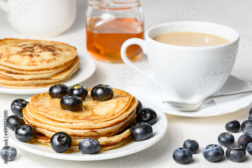 Pancakes with blueberry on white plate, creamer and teacup on white table