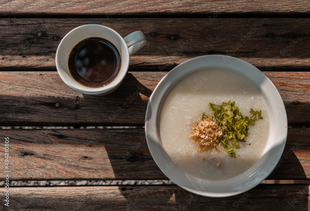 Pork congee or Rice porridge with minced pork sprinkled with deep-fried garlic and coriander in white bowl Served with cup of black coffee on old wooden table for new morning. Asia breakfast, Pork congee or Rice porridge with minced pork sprinkled with deep-fried garlic and coriander in white bowl Served with cup of black coffee on old wooden table for new morning. Asia breakfast,
