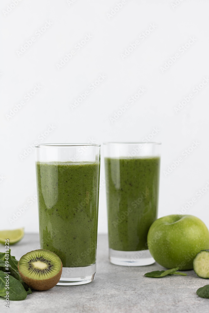Green detox smoothie in a glass on a grey background, copy space. Green smoothie of spinach, kiwi, banana, apple in a glass. Green detox smoothie in a glass on a grey background, copy space. Green smoothie of spinach, kiwi, banana, apple in a glass.