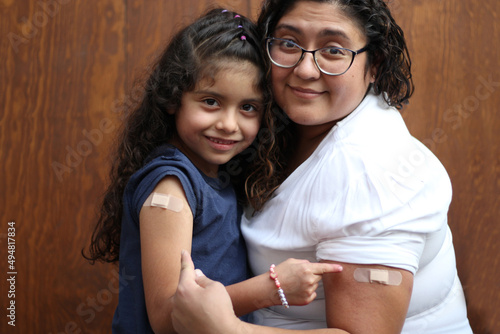 Happy and hugging Latin mom and daughter show their recently vaccinated arms against Covid-19 in the new normality due to the Coronavirus pandemic
 photo