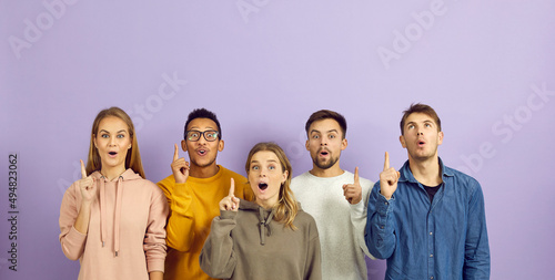 Group of happy young diverse multiethnic people surprised by bright idea and solution standing on purple color background and pointing index fingers up with open mouths and surprised face expressions photo