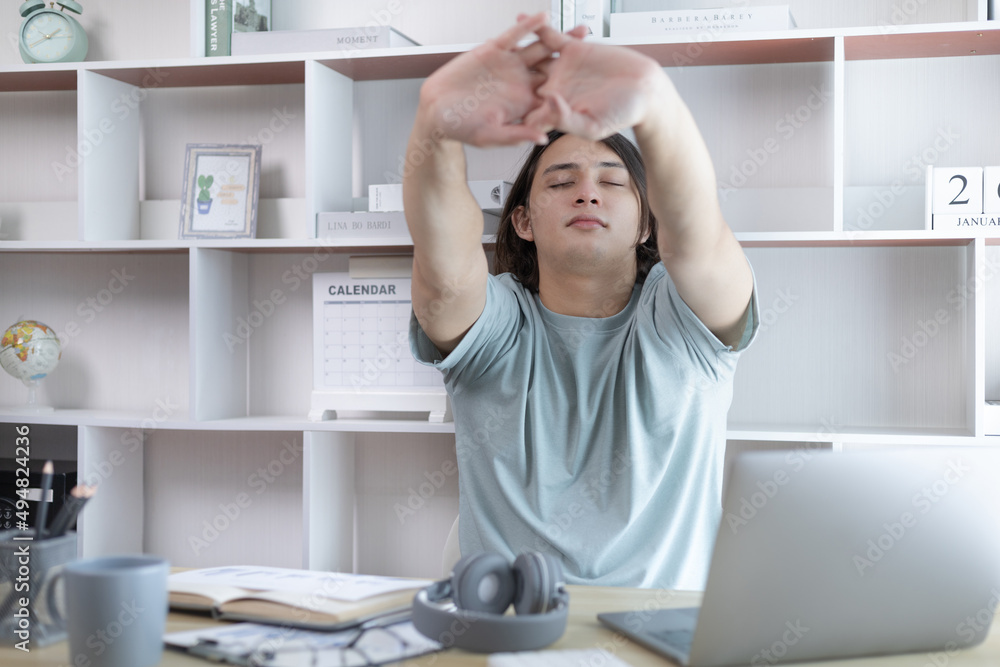 Young Asian male employee is doing a relaxing posture after a hard Midday's work, Happy men resting at work after work is finished, Fatigue is eased, Men working at home, Relax, Attractive, Success. Young Asian male employee is doing a relaxing posture after a hard Midday's work, Happy men resting at work after work is finished, Fatigue is eased, Men working at home, Relax, Attractive, Success.