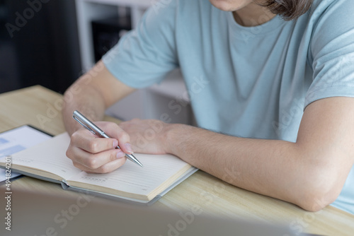 Asian man taking notes in notebook while studying online in laptop at home, Video chat, Online communication , Stay home, New normal, Distance learning.., Social distancing, Learn online...
