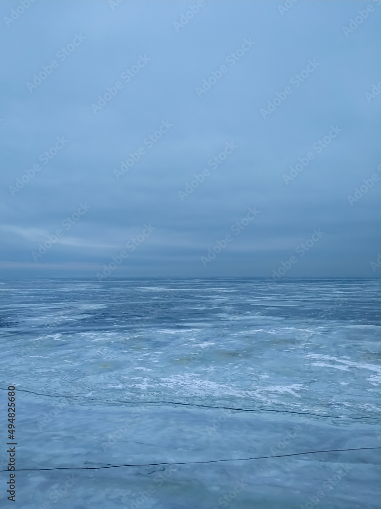 A frozen icy river and a cloudy sky in a single color connected on the horizon line.