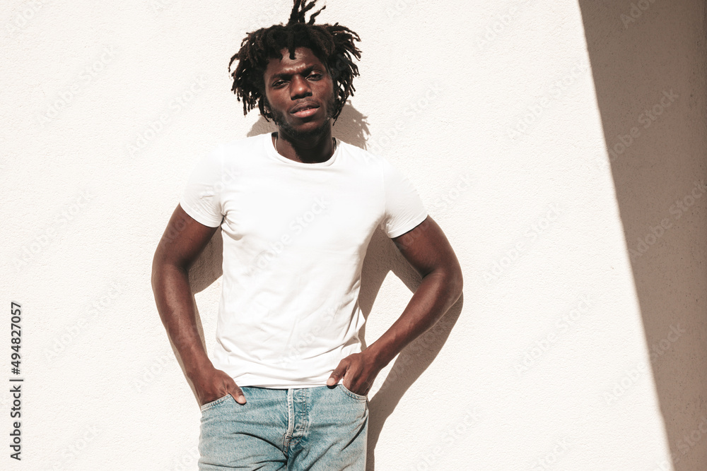 Portrait of handsome hipster  African man dressed in white  summer t-shirt and jeans. Fashion male with dreadlocks hairstyle posing  near white wall in the street Stock Photo | Adobe Stock